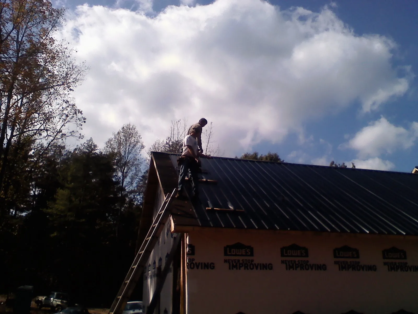Roofer fastening dark metal panels high against a cloudy sky, from a Roof Inspection job in Fairfax