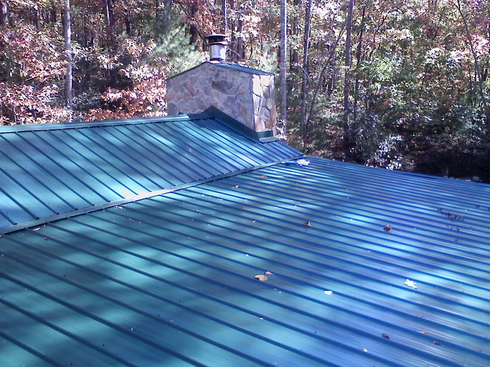 New green metal roof and stone chimney surrounded by autumn woods in Fairfax