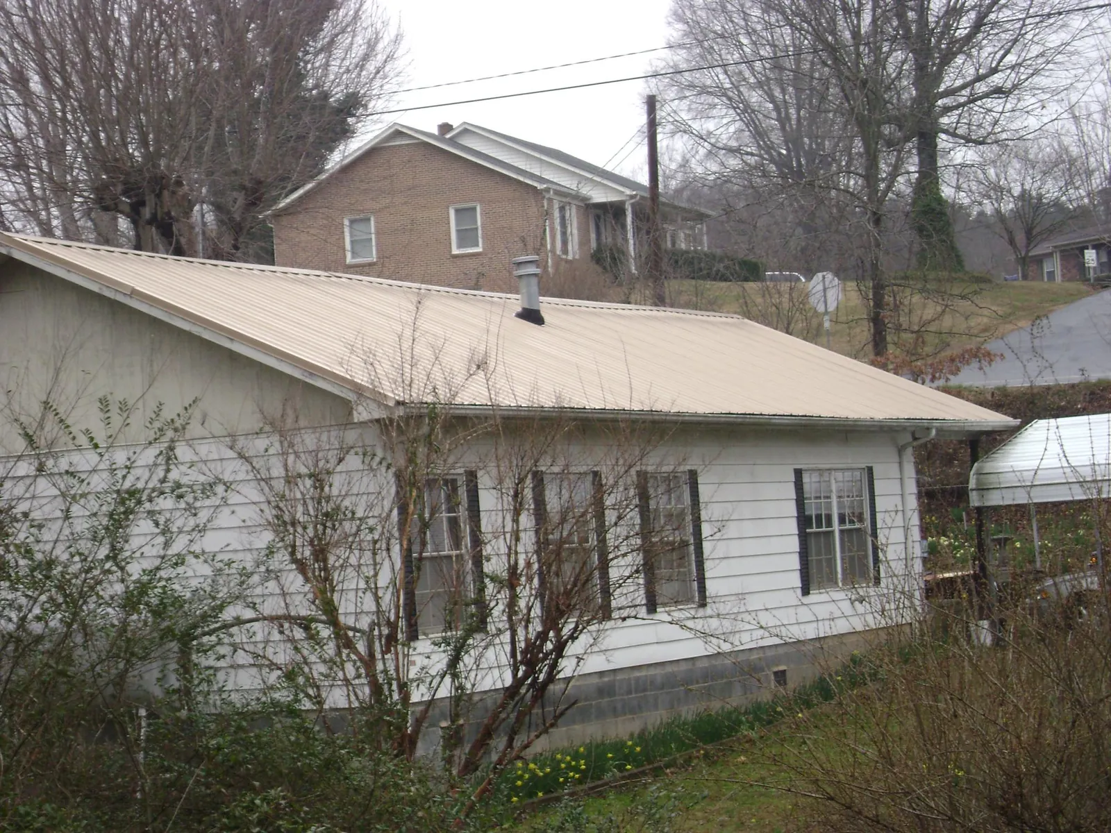 Tan metal roof on a white sided house set into a hillside — Commercial Roofing by Roofing Brothers in Fairfax